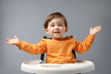 Photo of Cute little kid with spoon sitting in high chair on light grey background