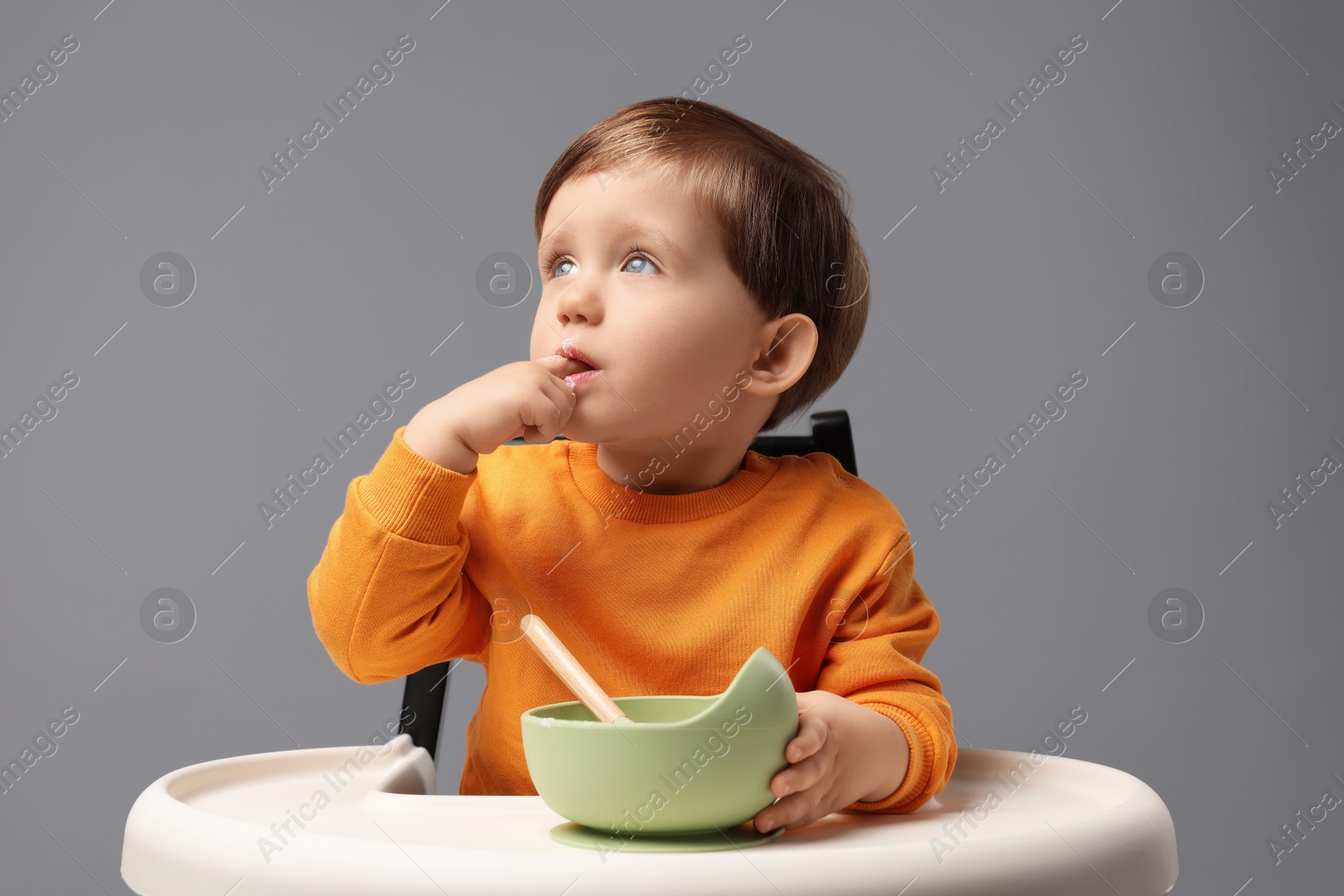 Photo of Cute little kid eating healthy baby food from bowl in high chair on light grey background