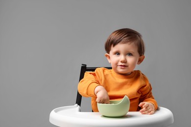 Photo of Cute little kid eating healthy baby food from bowl in high chair on light grey background