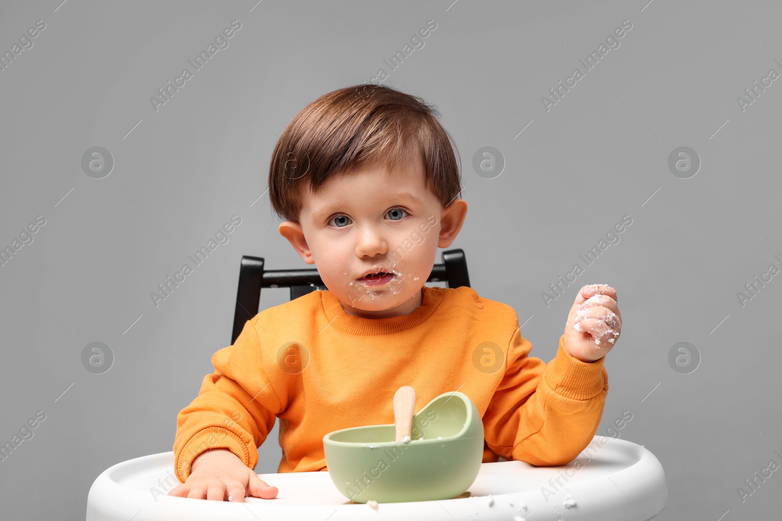 Photo of Cute little kid eating healthy baby food from bowl in high chair on light grey background