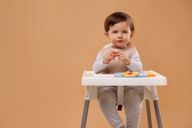 Photo of Healthy baby food. Cute little kid eating fruits in high chair on beige background, space for text