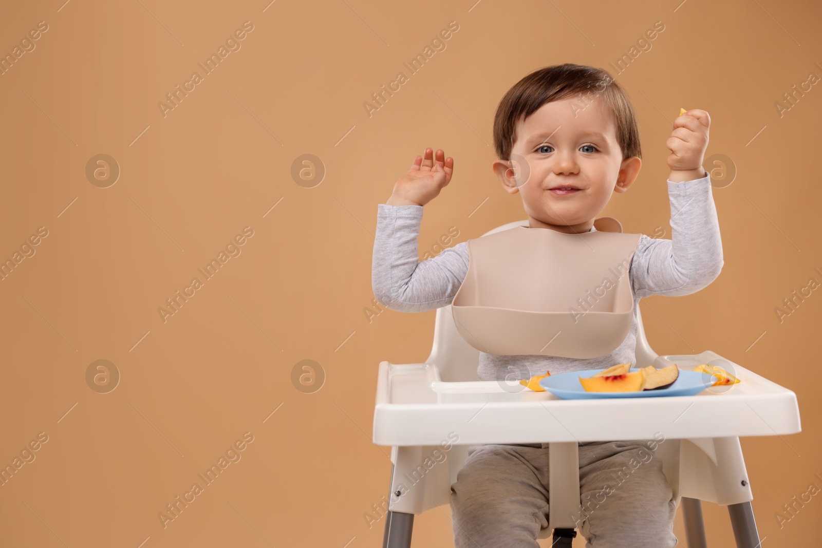 Photo of Healthy baby food. Cute little kid eating fruits in high chair on beige background, space for text