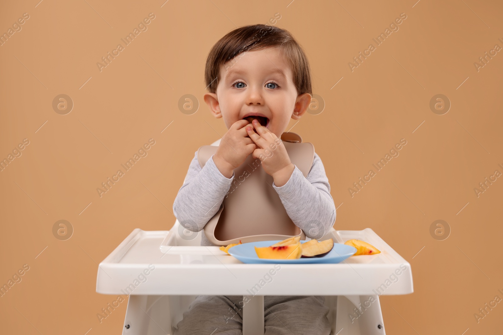 Photo of Healthy baby food. Cute little kid eating fruits in high chair on beige background