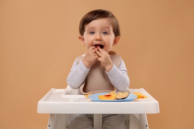 Photo of Healthy baby food. Cute little kid eating fruits in high chair on beige background