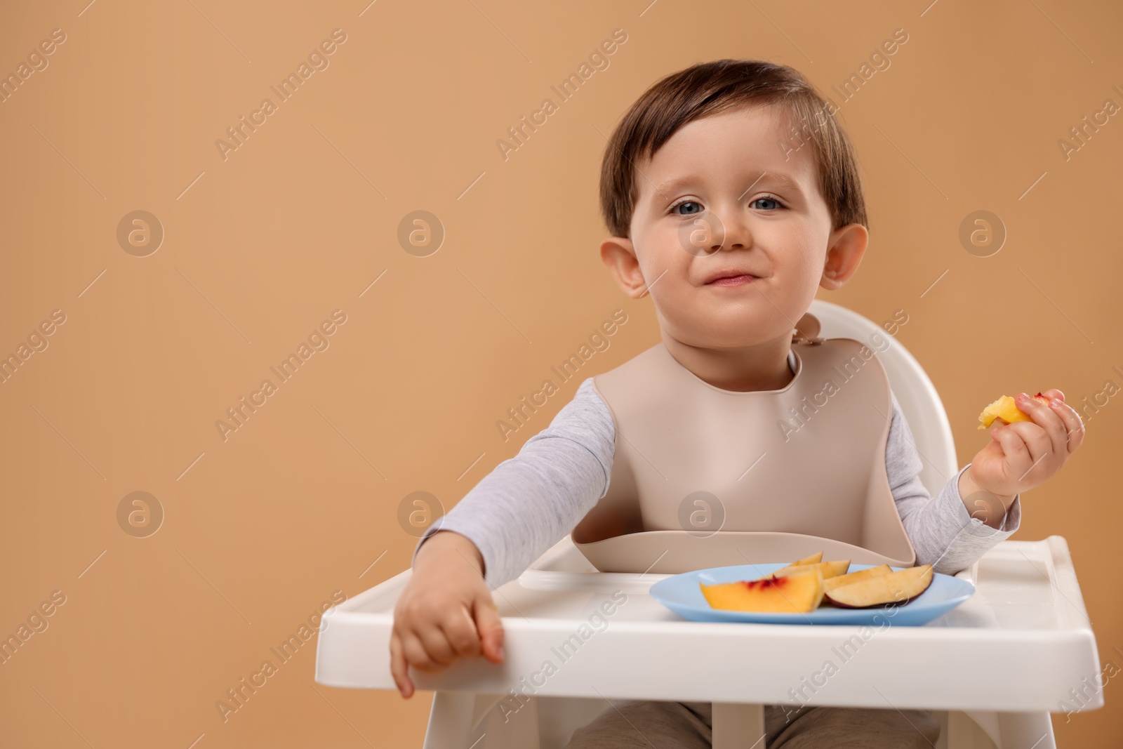 Photo of Healthy baby food. Cute little kid eating fruits in high chair on beige background, space for text