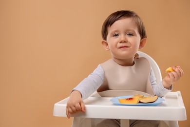 Photo of Healthy baby food. Cute little kid eating fruits in high chair on beige background, space for text