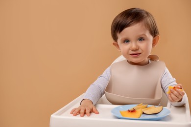 Photo of Healthy baby food. Cute little kid eating fruits in high chair on beige background, space for text