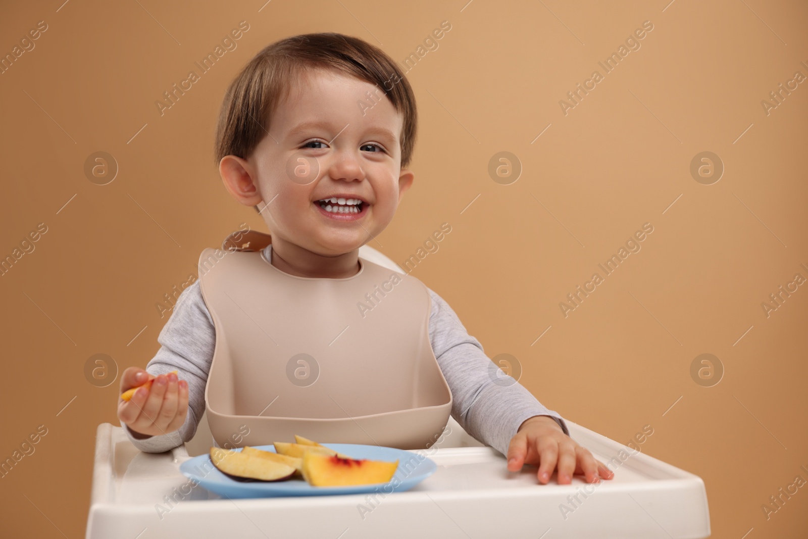 Photo of Healthy baby food. Cute little kid eating fruits in high chair on beige background