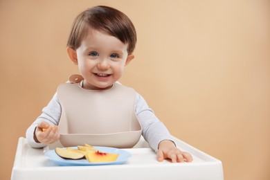 Photo of Healthy baby food. Cute little kid eating fruits in high chair on beige background, space for text