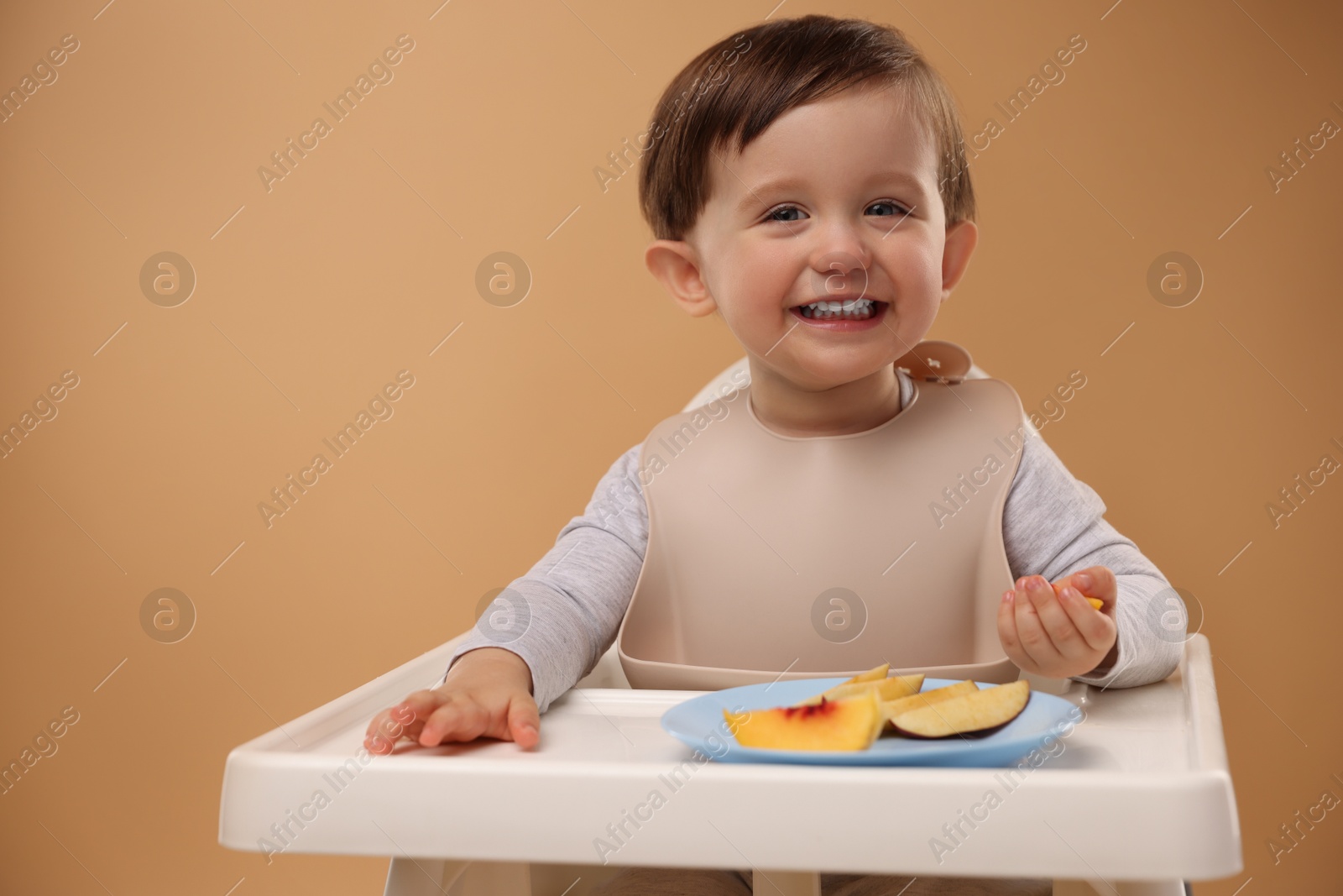 Photo of Healthy baby food. Cute little kid eating fruits in high chair on beige background, space for text