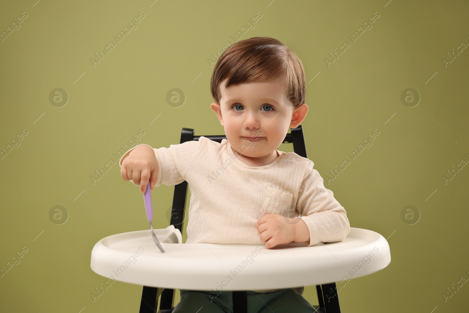 Photo of Cute little kid with fork sitting in high chair on olive background