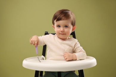 Photo of Cute little kid with fork sitting in high chair on olive background