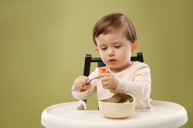 Photo of Cute little baby eating healthy food from bowl in high chair on olive background, space for text