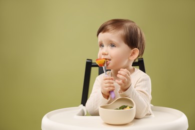 Photo of Cute little baby eating healthy food from bowl in high chair on olive background