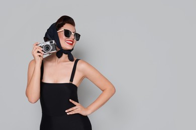 Photo of Pin-up woman in sunglasses with camera on grey background, space for text