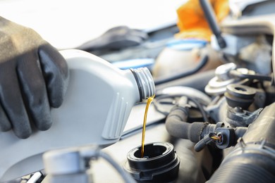 Photo of Man pouring motor oil into car engine, closeup