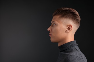 Photo of Handsome young man with stylish haircut on black background. Space for text