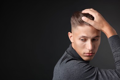 Photo of Confident young man with stylish haircut on black background. Space for text