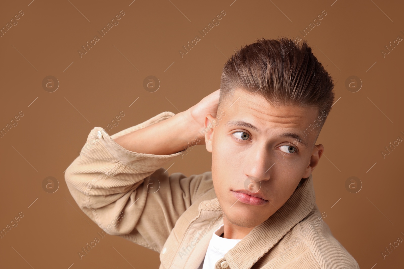 Photo of Confident young man with stylish haircut on brown background