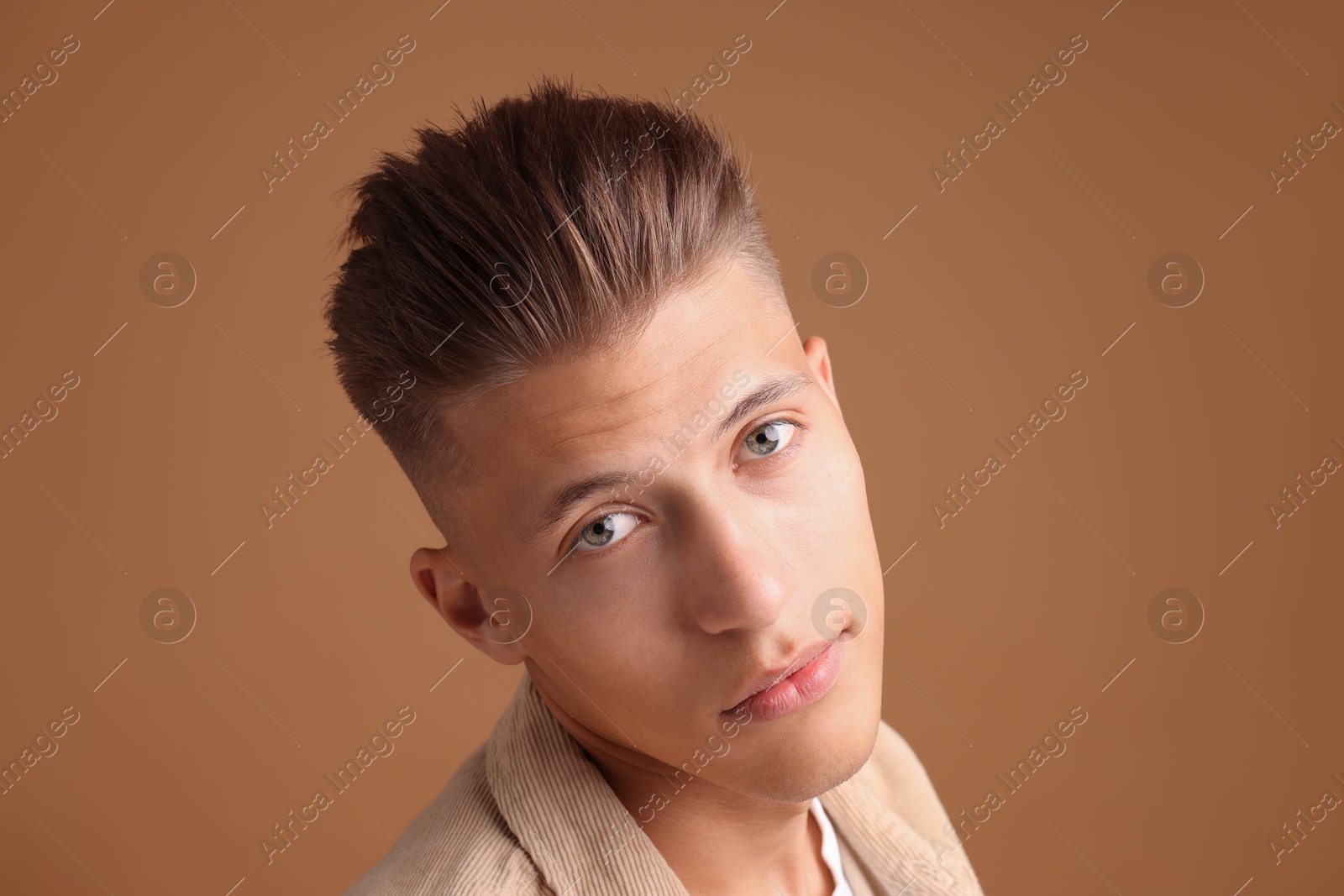 Photo of Confident young man with stylish haircut on brown background