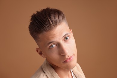 Photo of Confident young man with stylish haircut on brown background