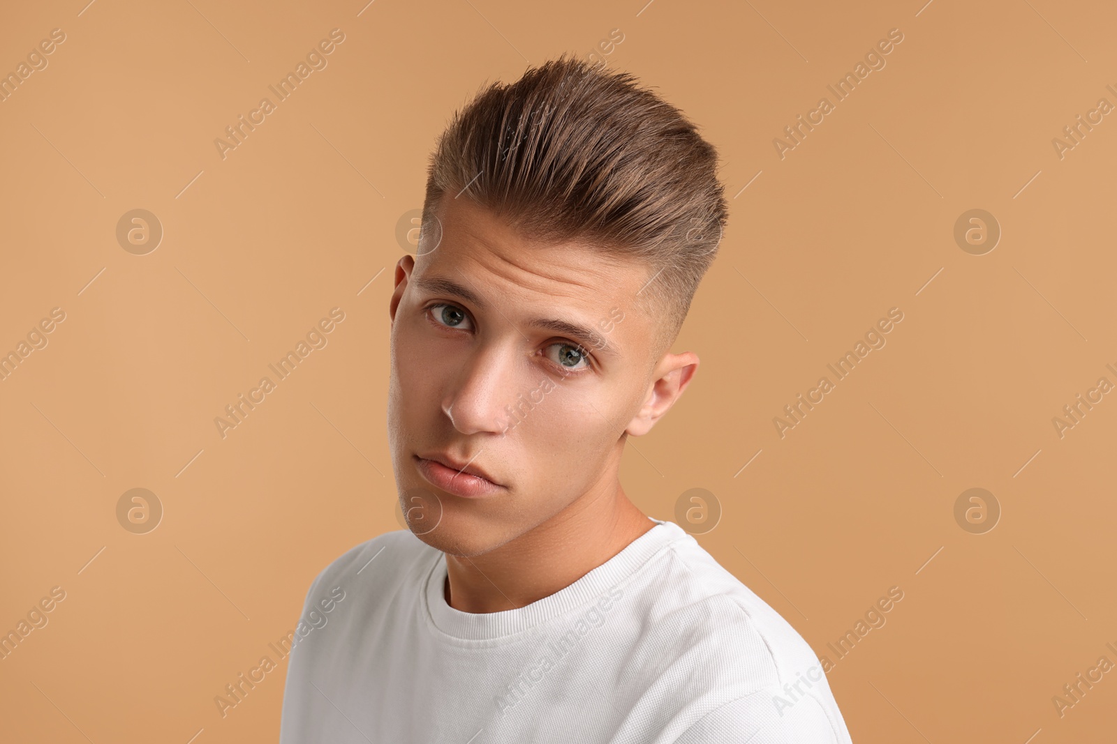 Photo of Confident young man with stylish haircut on light brown background