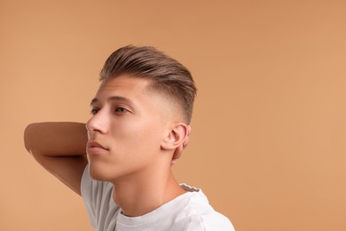 Photo of Confident young man with stylish haircut on light brown background. Space for text