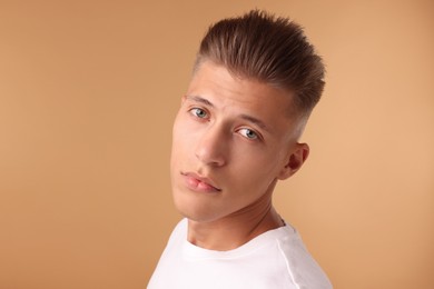 Photo of Confident young man with stylish haircut on light brown background