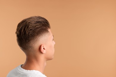 Photo of Young man with stylish haircut on light brown background. Space for text