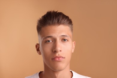 Photo of Confident young man with stylish haircut on light brown background