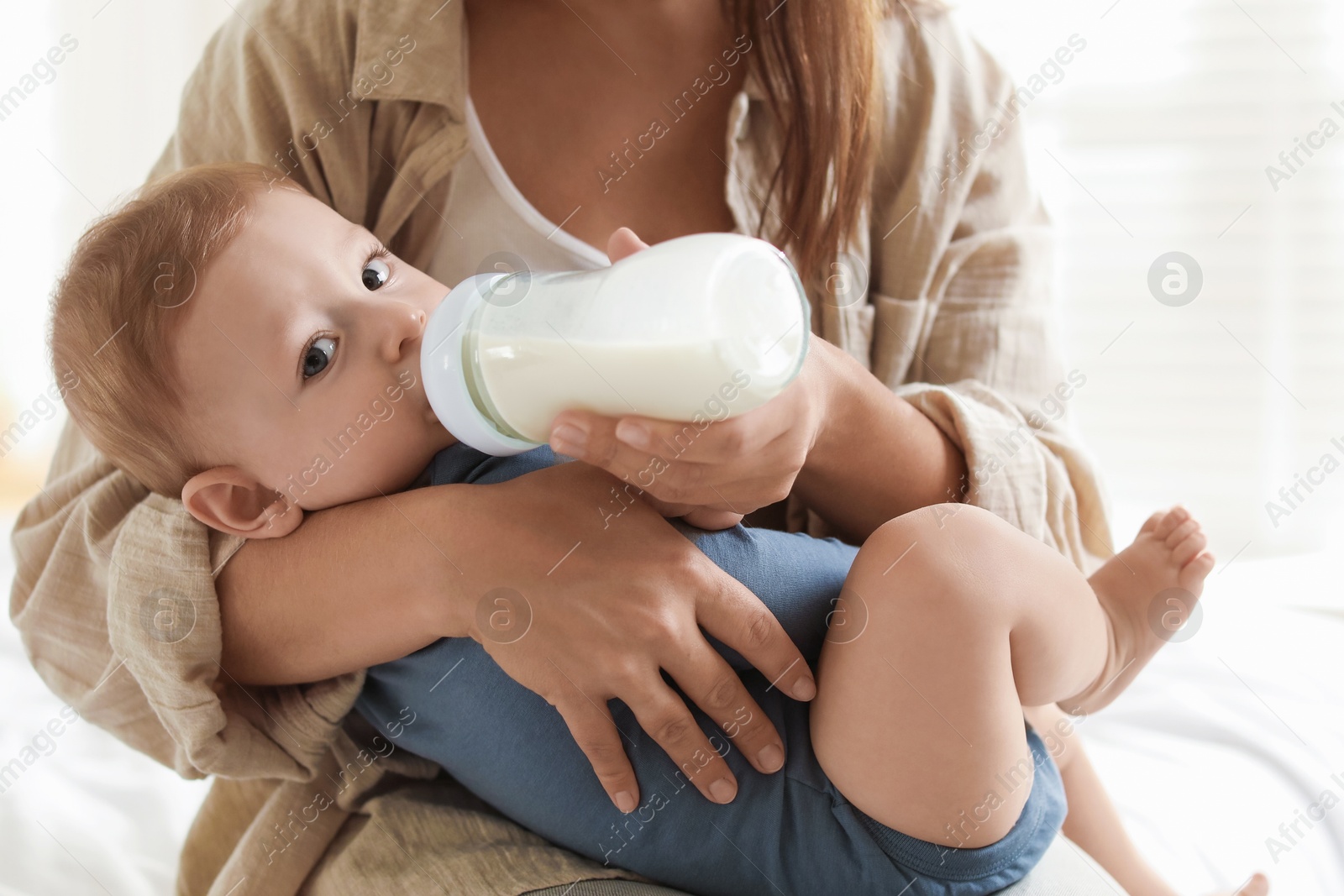 Photo of Mother feeding her little baby from bottle on bed indoors, closeup