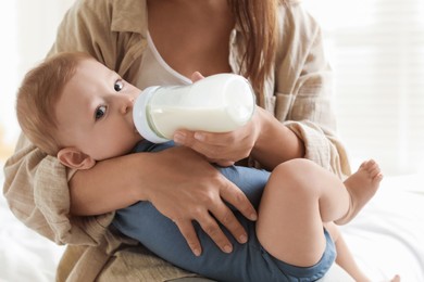 Mother feeding her little baby from bottle on bed indoors, closeup