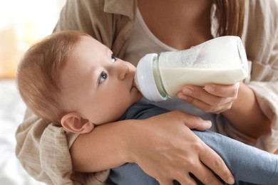 Photo of Mother feeding her little baby from bottle on bed indoors, closeup