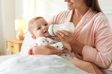 Photo of Mother feeding her little baby from bottle on bed at home, closeup