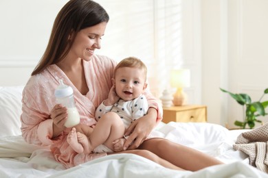 Photo of Mother holding cute little baby and bottle of milk on bed at home. Space for text