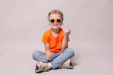 Photo of Little boy with sunglasses listening to music and showing rock gesture on light grey background