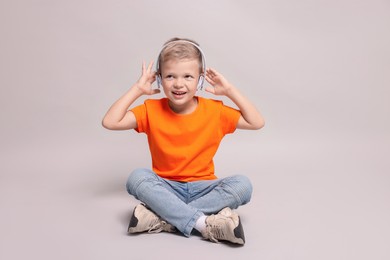 Little boy listening to music on light grey background