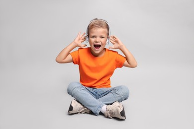 Little boy listening to music on light grey background