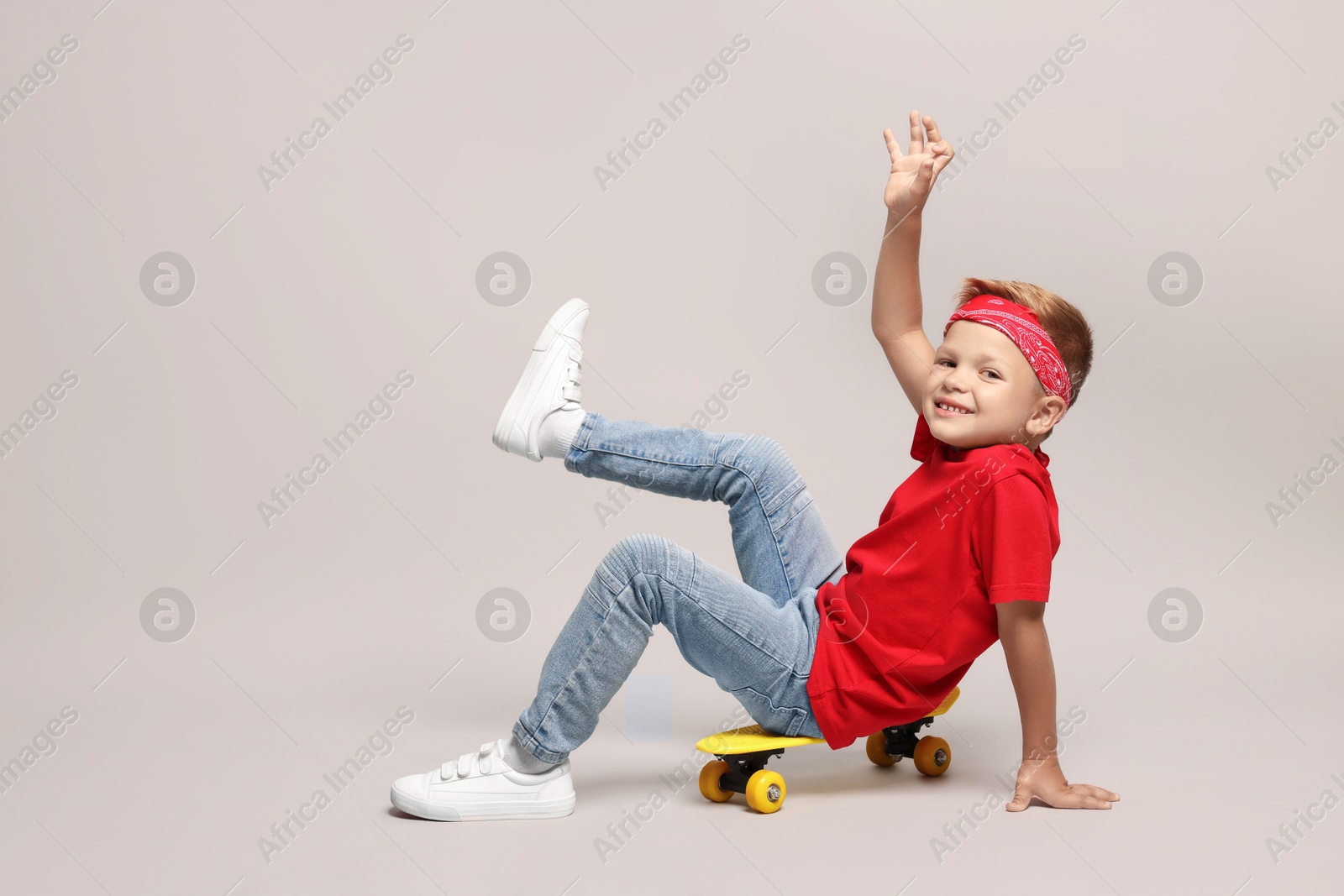 Photo of Little boy with skateboard on light grey background, space for text