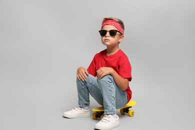 Little boy with sunglasses and skateboard on light grey background