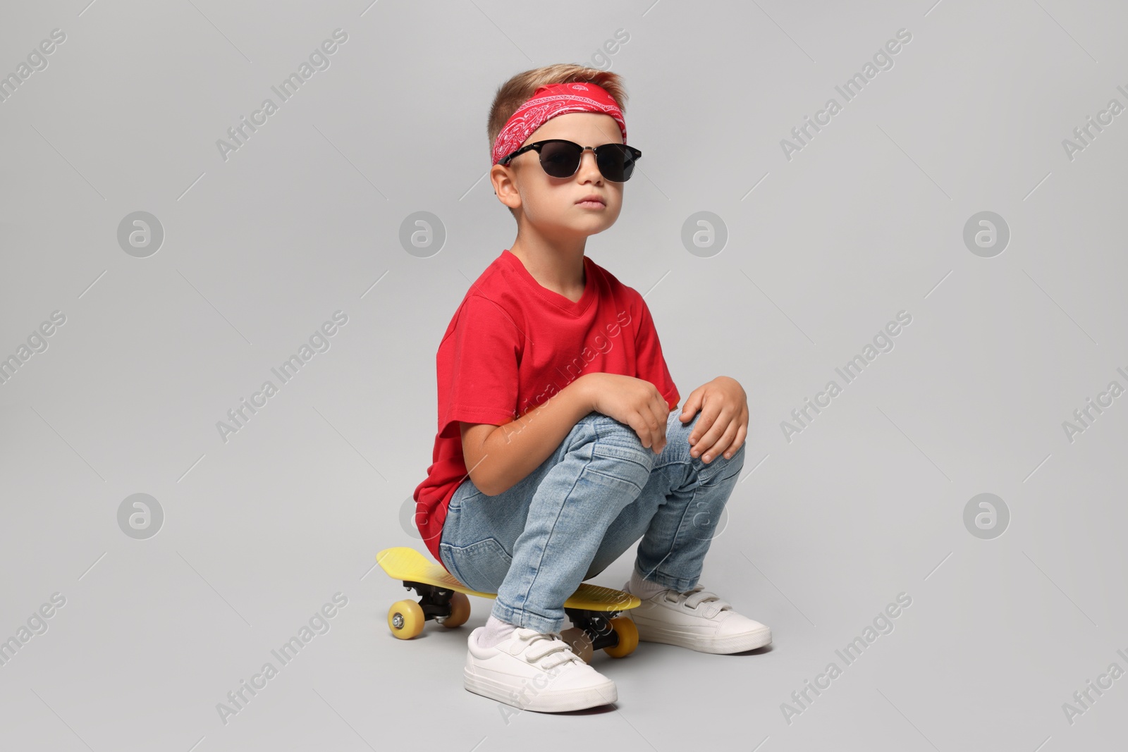 Photo of Little boy with sunglasses and skateboard on light grey background