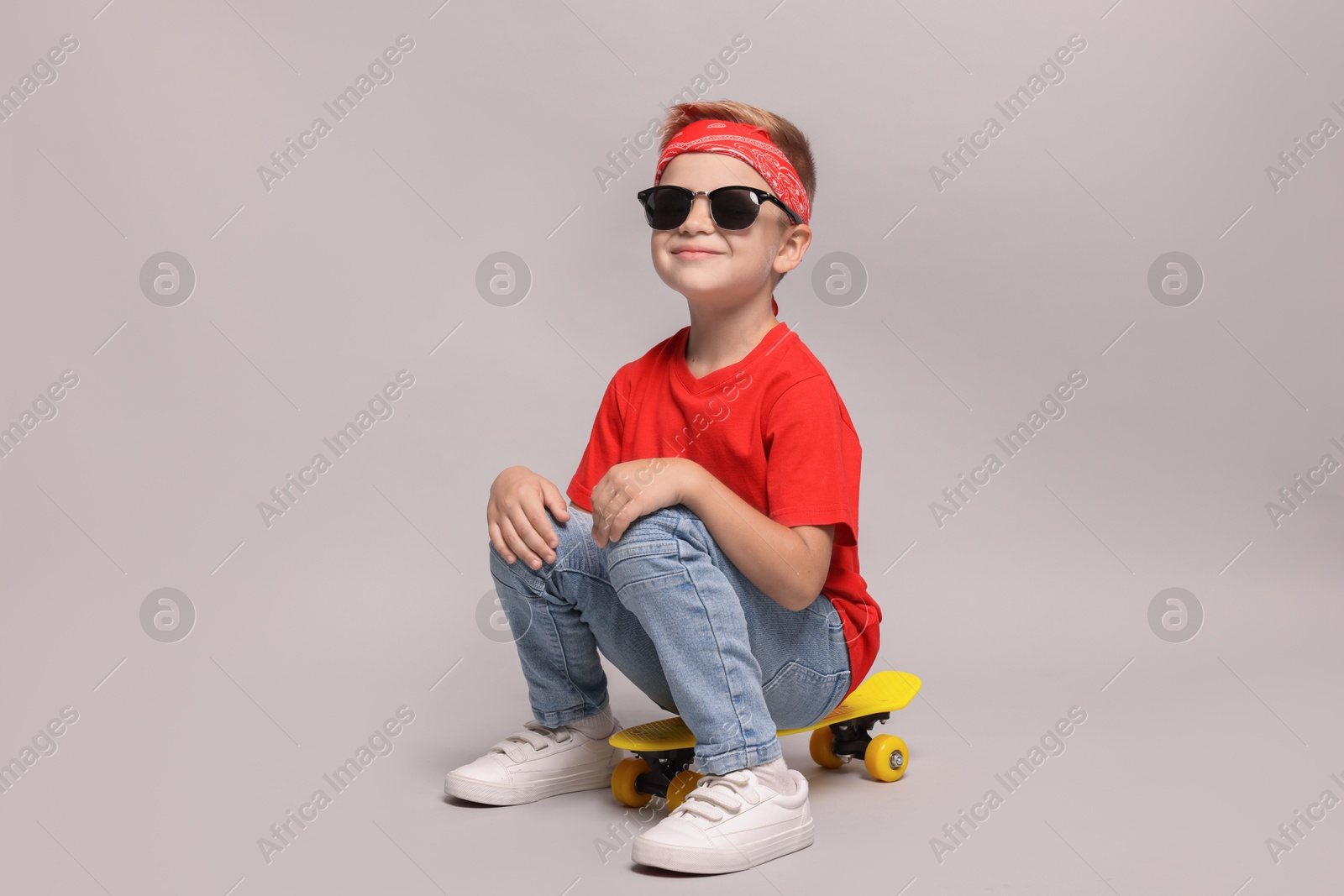 Photo of Little boy with sunglasses and skateboard on light grey background