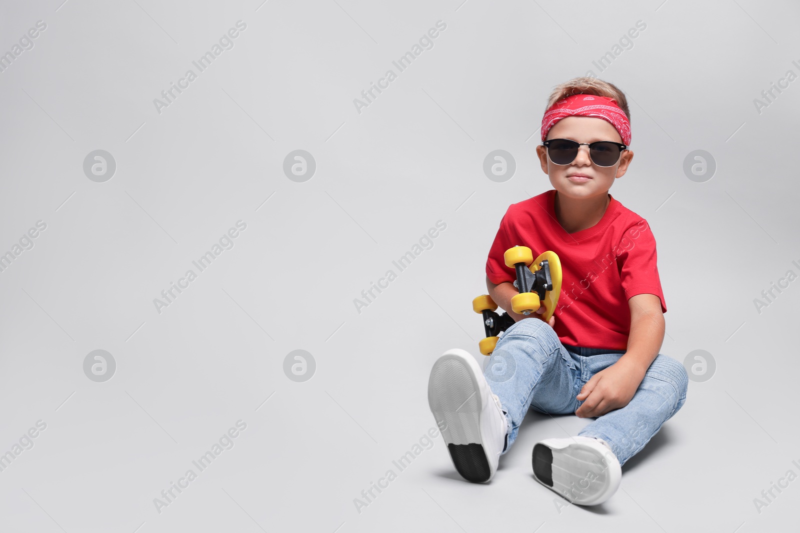 Photo of Little boy with sunglasses and skateboard on light grey background, space for text