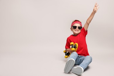 Little boy with sunglasses and skateboard on light grey background, space for text