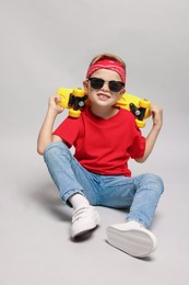 Photo of Little boy with sunglasses and skateboard on light grey background