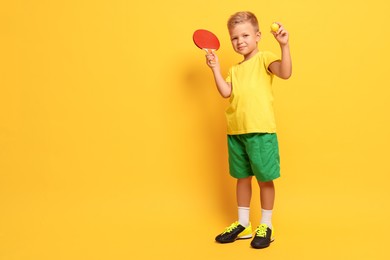 Photo of Little boy with ping pong racket and ball on orange background, space for text