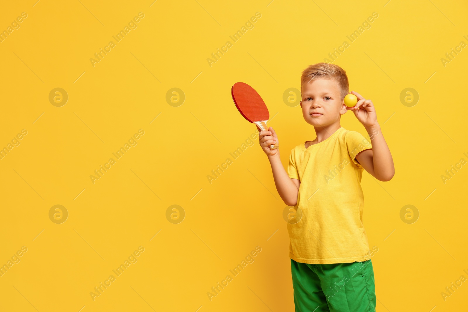 Photo of Little boy with ping pong racket and ball on orange background, space for text