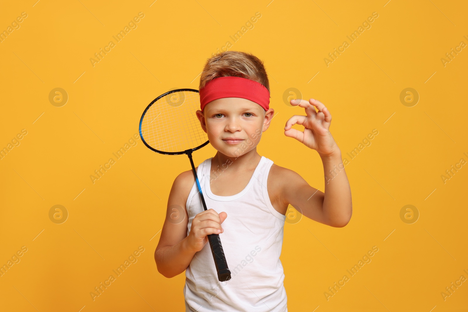 Photo of Little boy with badminton racket showing ok gesture on orange background