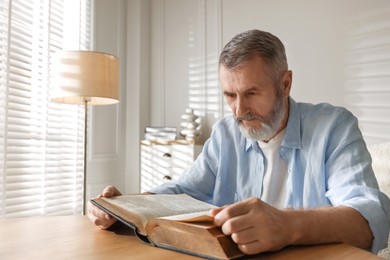 Photo of Senior man reading book at table indoors