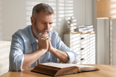 Photo of Senior man reading book at table indoors